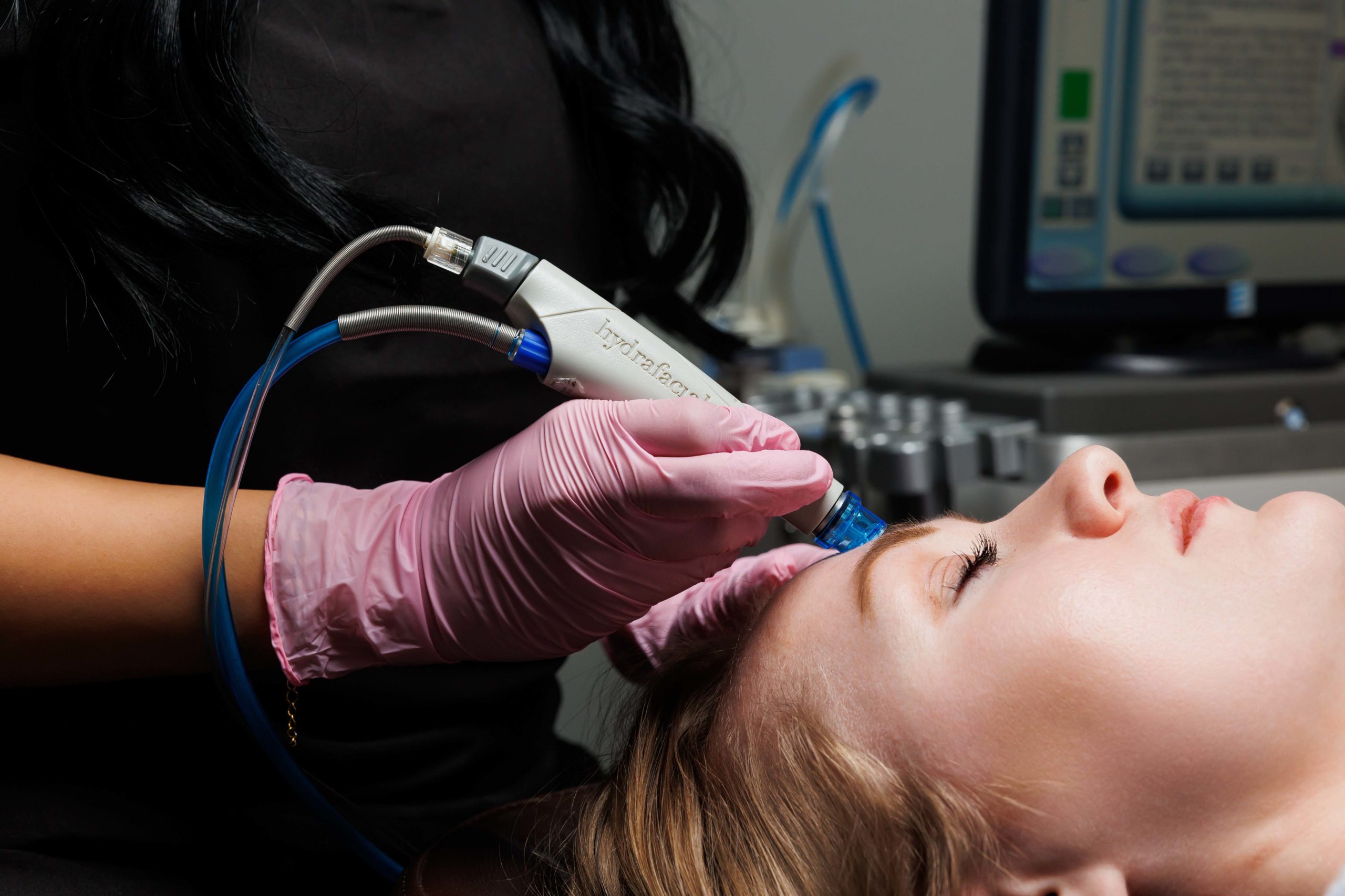 Cosmetologist holding device and woman's face in hand Getting Hydrafacial Treatment | APEX Performance & Aesthetics in Sandy, UT